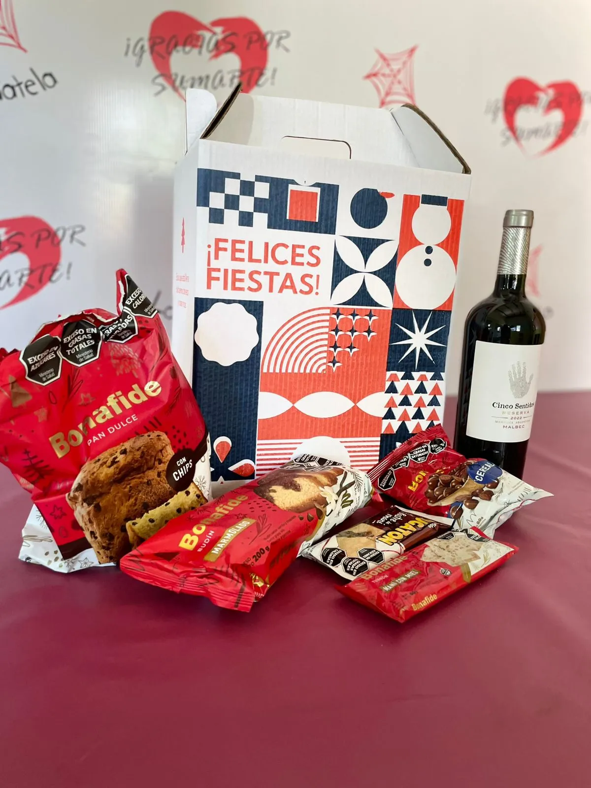 Caja de cartón navideña "¡Felices Fiestas!" con pan dulce, budín, turrón, chocolates y una botella de vino