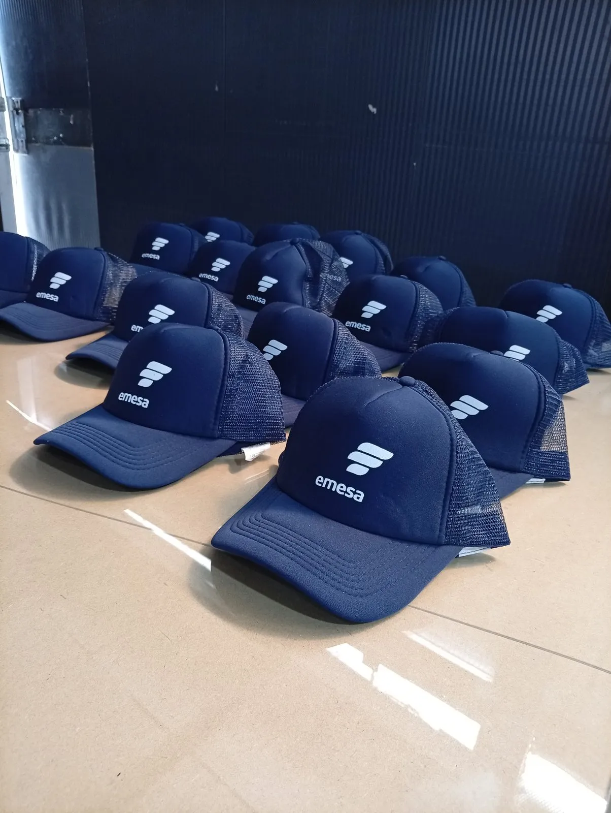 Gorras trucker azul marino con logo estampado, alineadas sobre el piso del taller